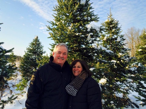Pastors Kevin and Melodie Carlson standing outdoors in front of fir trees