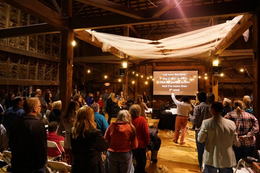 People gathered for worship beneath warm lights at an Albany Worships barn event